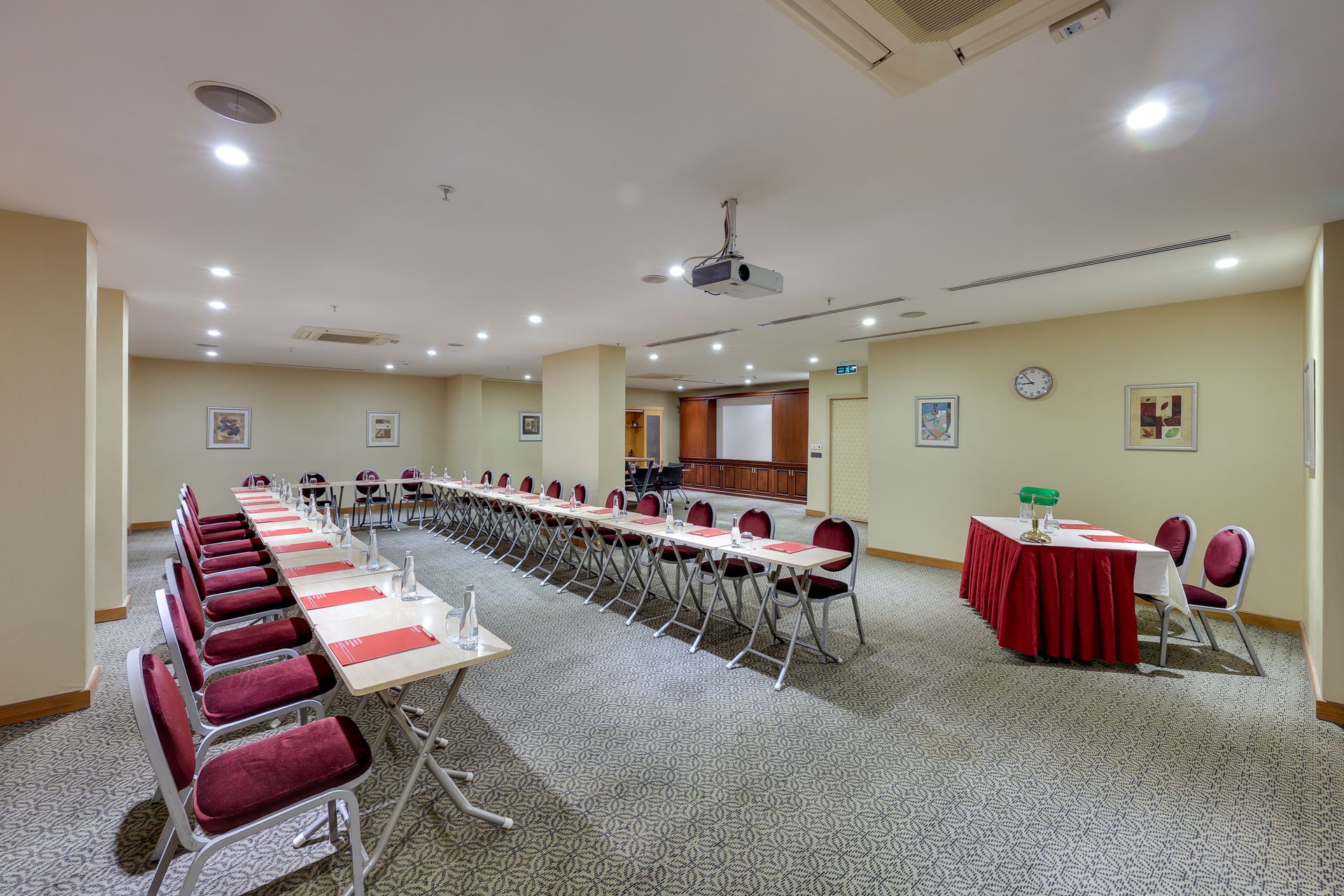 Conference room with U-shaped tables, red chairs, and a small table with a red tablecloth.