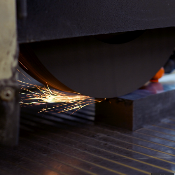Eine Schleifscheibe sprüht Funken, während sie einen dunklen Metallblock auf dem Fabrikboden schärft.