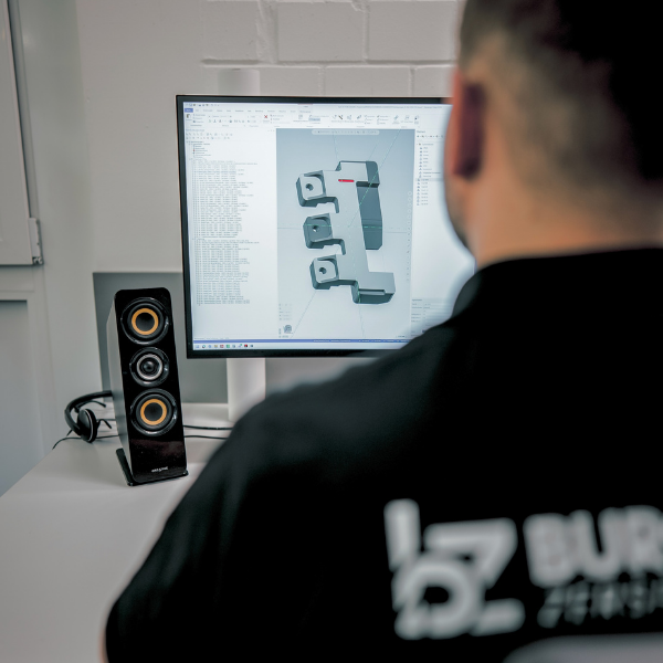 Hände halten ein Metallteil und vergleichen es mit einem 3D-Modell auf einem Computerbildschirm.