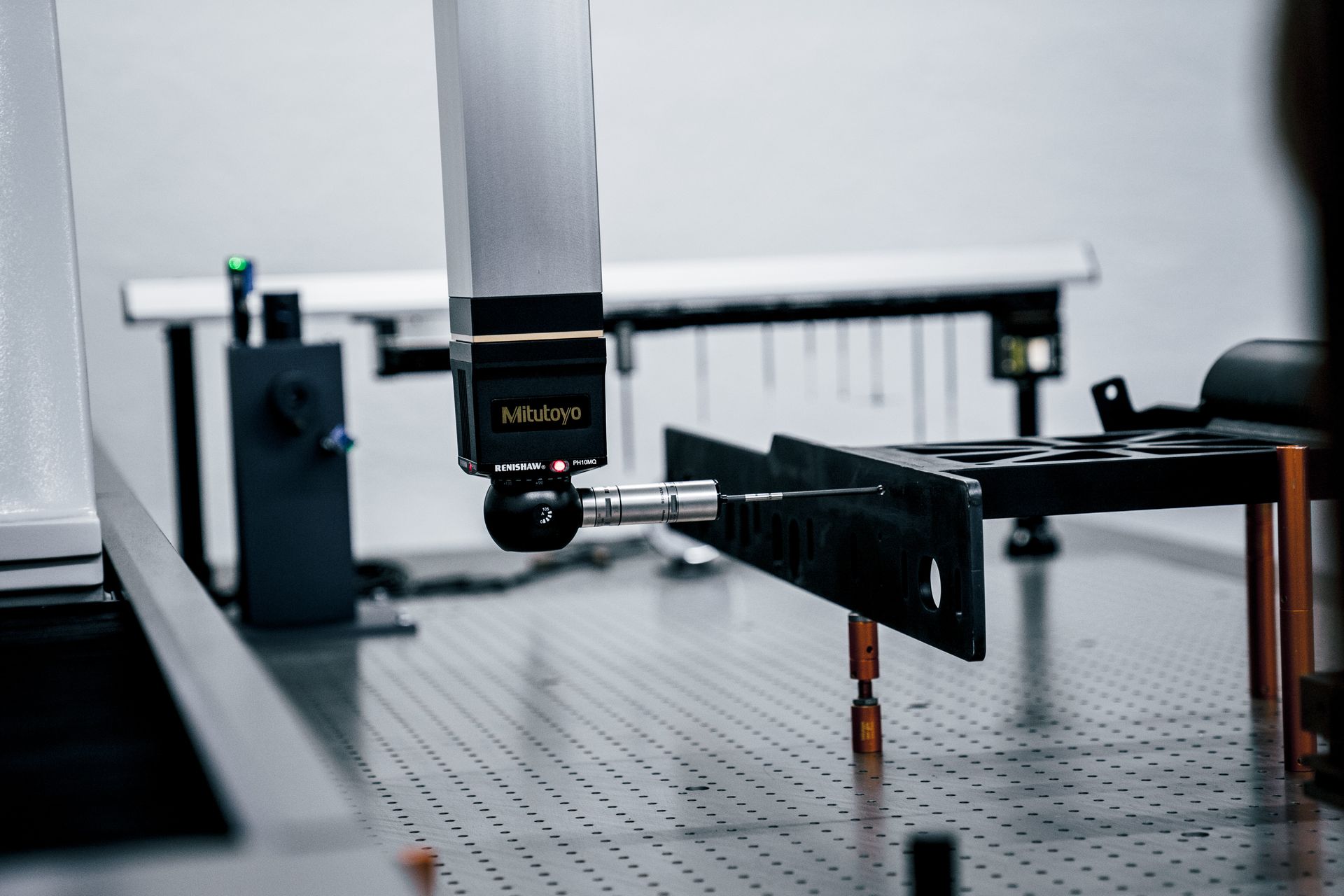 Ein Roboterarm vermisst ein schwarzes Metallteil auf einer grauen Plattform in einer industriellen Umgebung.