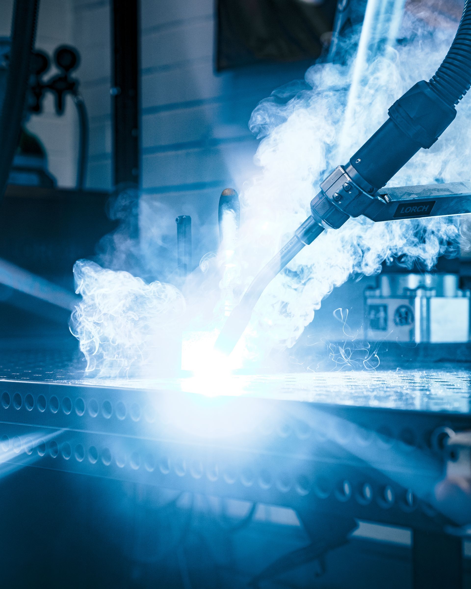 Roboterarm schweißt Metall, hellblaues Licht, Funken und Dampf.