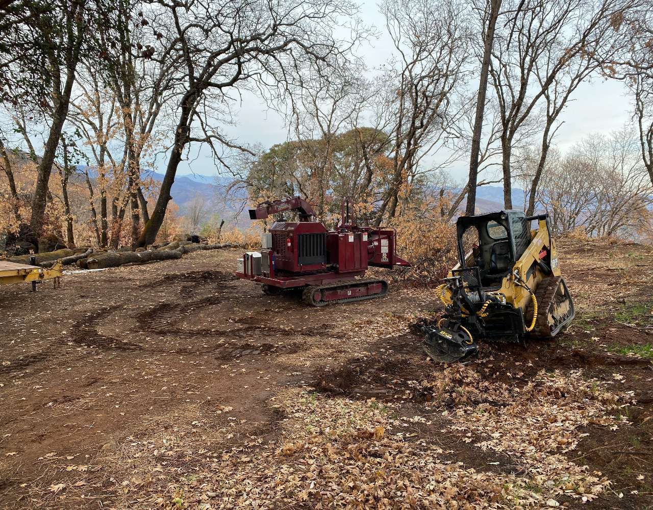 Two tractors are sitting in a field with trees in the background.