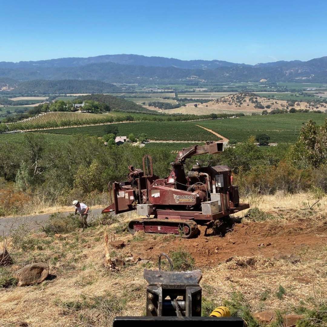Overturned rust-colored tractor in a dry hillside orchard with mountains in the background