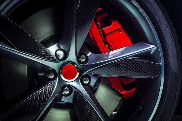 Close-up of a black carbon-fiber car wheel with a red brake caliper and red center cap Close-up of a black carbon-fiber car wheel with a red brake caliper and red center cap