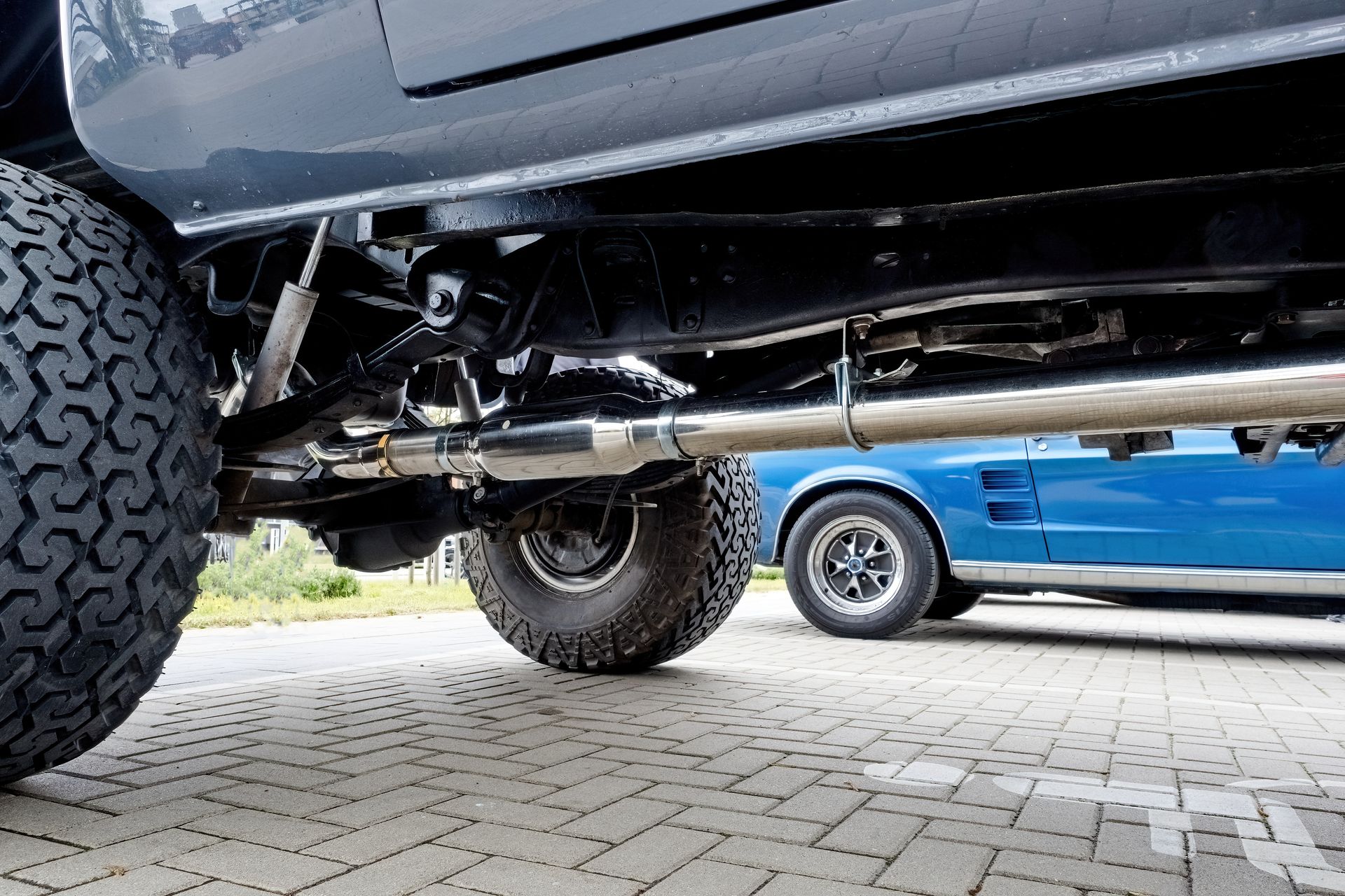 Low-angle view of a black truck undercarriage with large tires beside a blue vehicle on a paved lot Low-angle view of a black truck undercarriage with large tires beside a blue vehicle on a paved lot