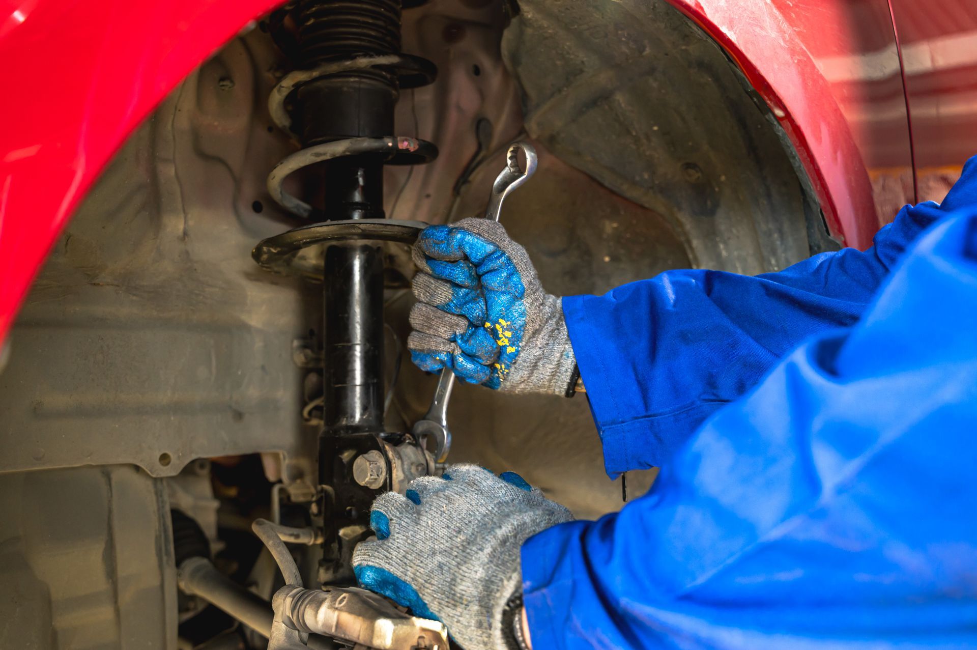 Mechanic in blue gloves working on a car suspension inside a wheel well Mechanic in blue gloves working on a car suspension inside a wheel well