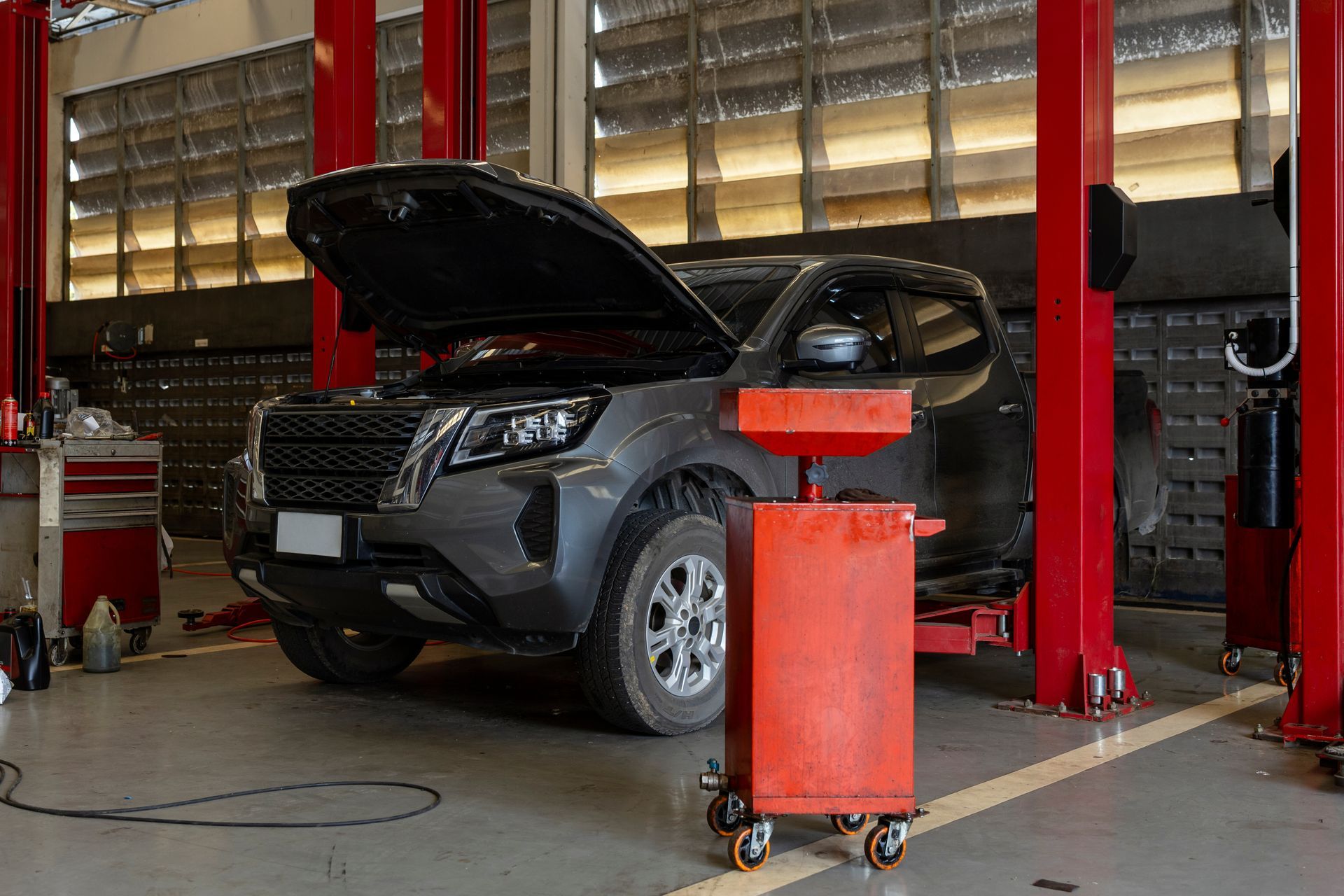 SUV with hood open in a car repair shop, near red vehicle lifts and a red tool cart SUV with hood open in a car repair shop, near red vehicle lifts and a red tool cart