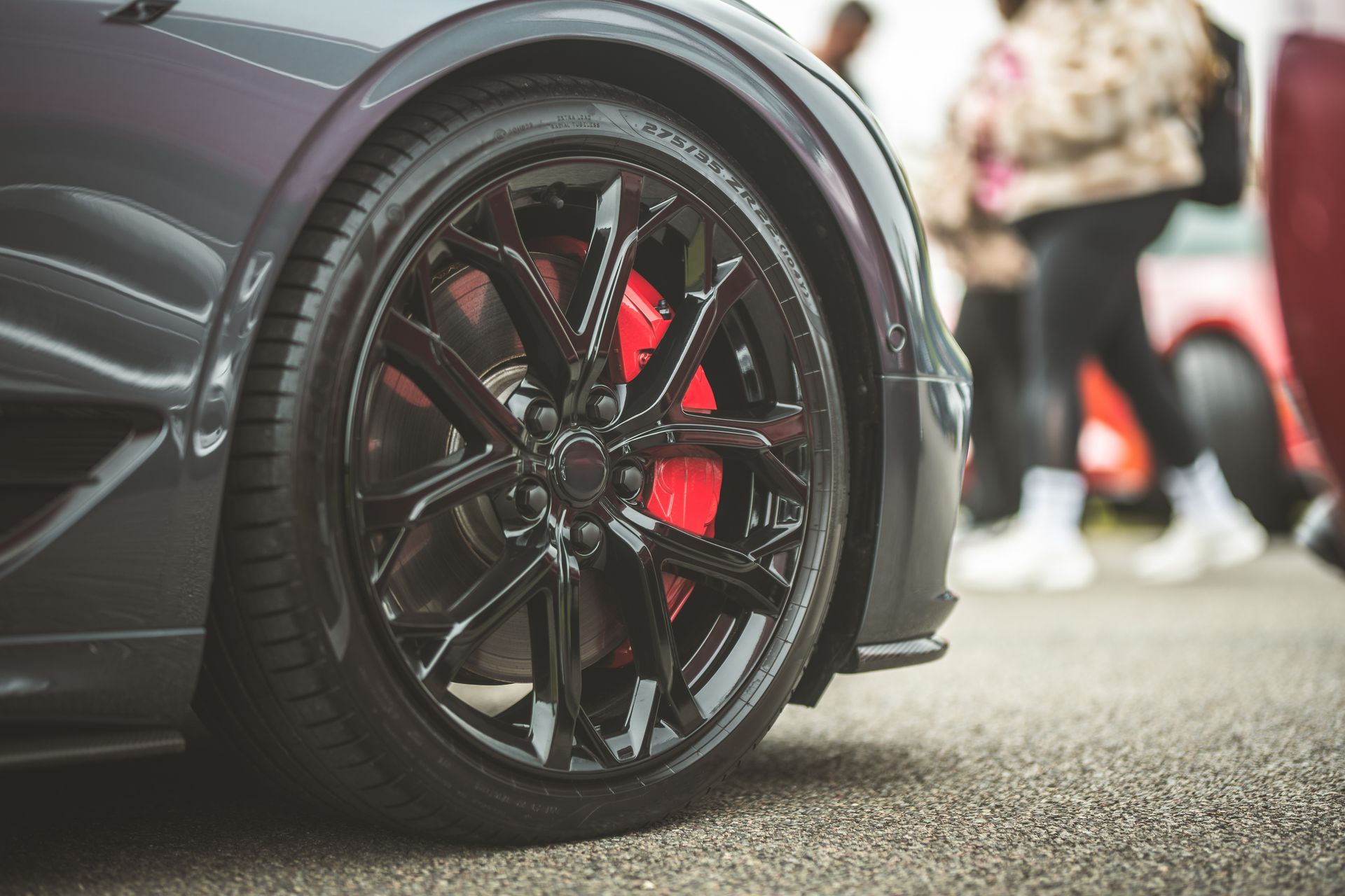 Close-up of a black sports car wheel with red brake caliper at a car show Close-up of a black sports car wheel with red brake caliper at a car show