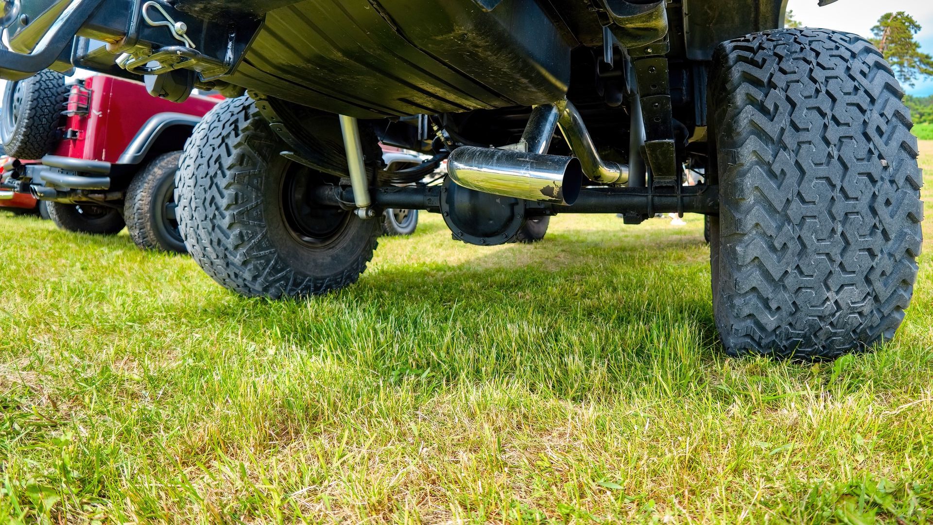 Low-angle view of off-road vehicle tires on grass, showing the undercarriage and suspension Low-angle view of off-road vehicle tires on grass, showing the undercarriage and suspension