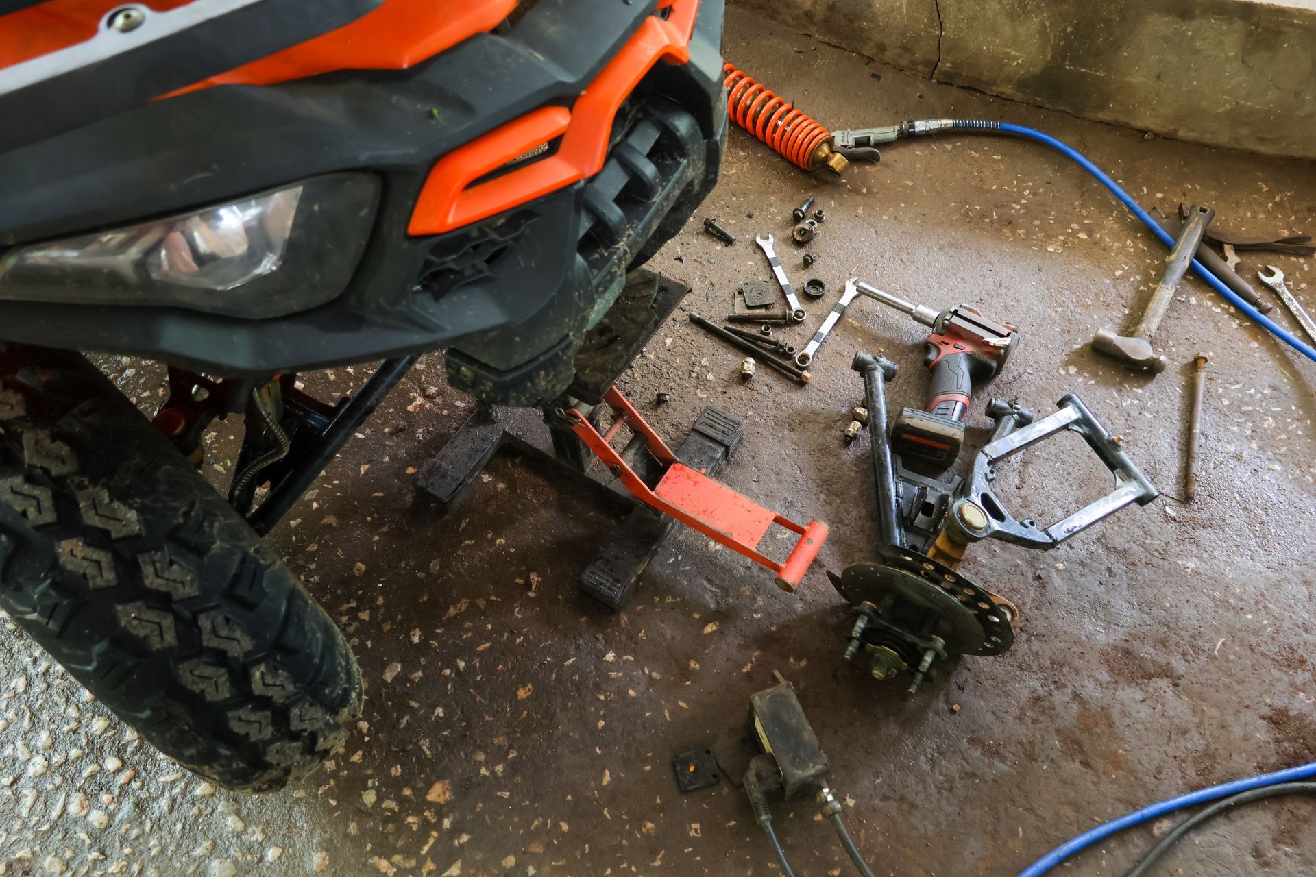 Orange ATV front end with tools and parts scattered on a garage floor during repairs Orange ATV front end with tools and parts scattered on a garage floor during repairs