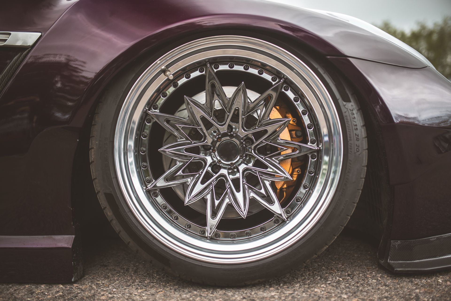 Close-up of a lowered purple car with a custom chrome star-spoke wheel and orange brake caliper Close-up of a lowered purple car with a custom chrome star-spoke wheel and orange brake caliper