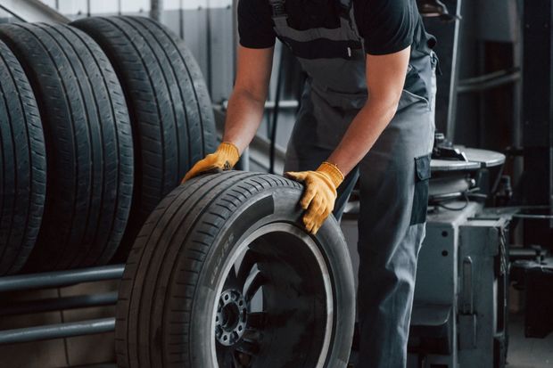 Mechanic in orange gloves handling a car tire in a workshop Mechanic in orange gloves handling a car tire in a workshop