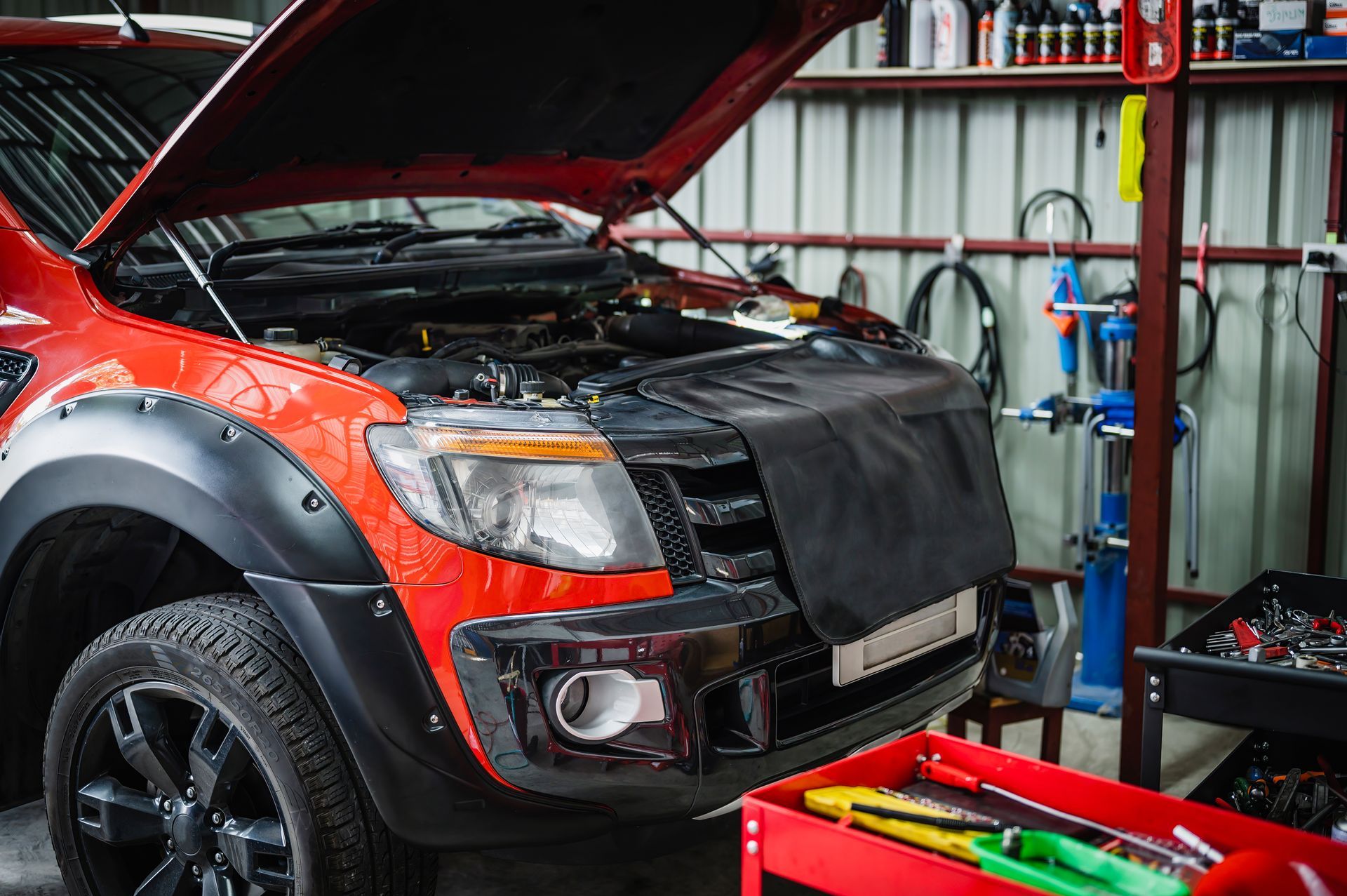 Red SUV with hood open in a garage, showing the front end during repairs Red SUV with hood open in a garage, showing the front end during repairs