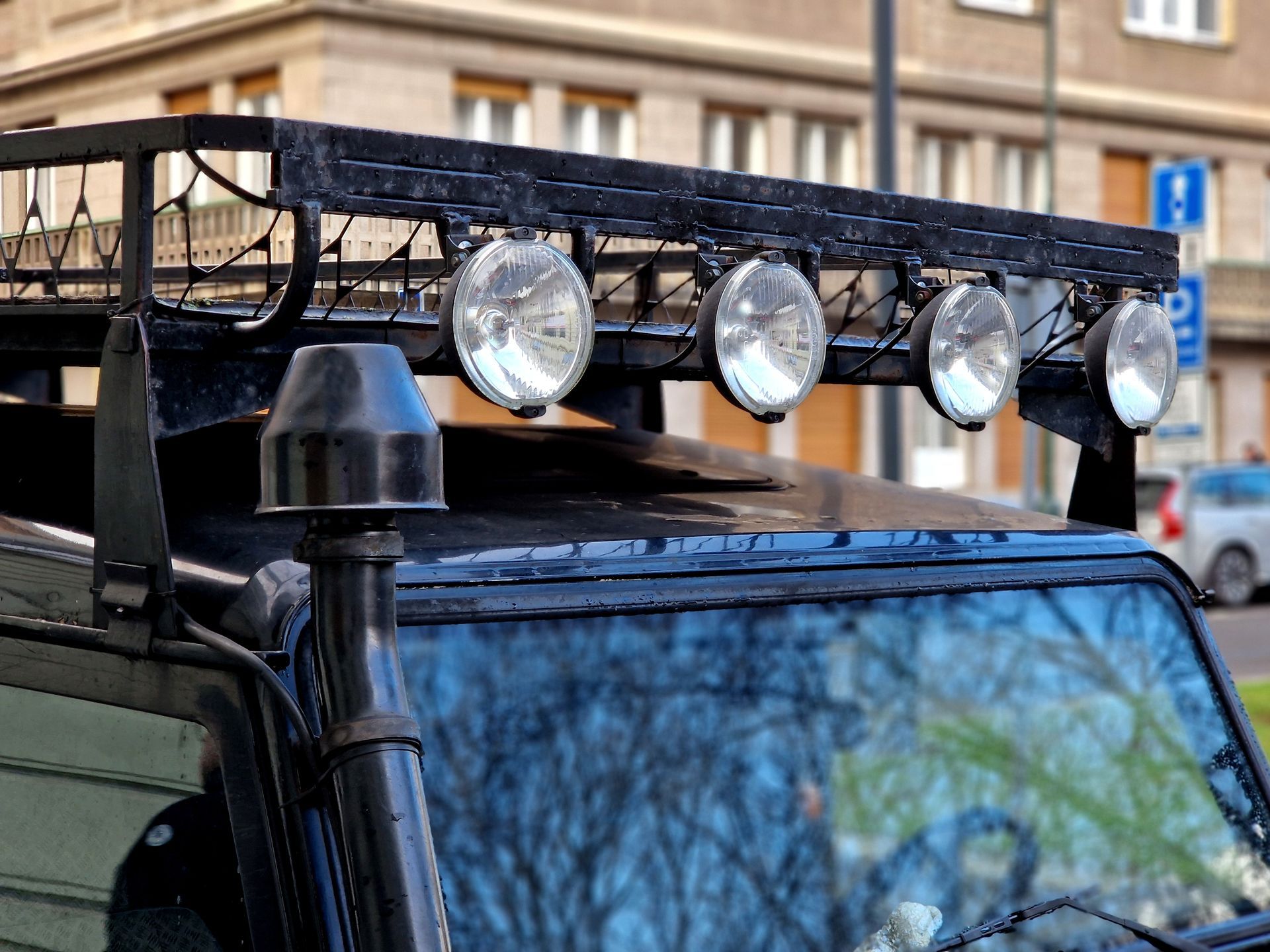 Black off-road vehicle with roof rack and four spotlights parked on a city street Black off-road vehicle with roof rack and four spotlights parked on a city street