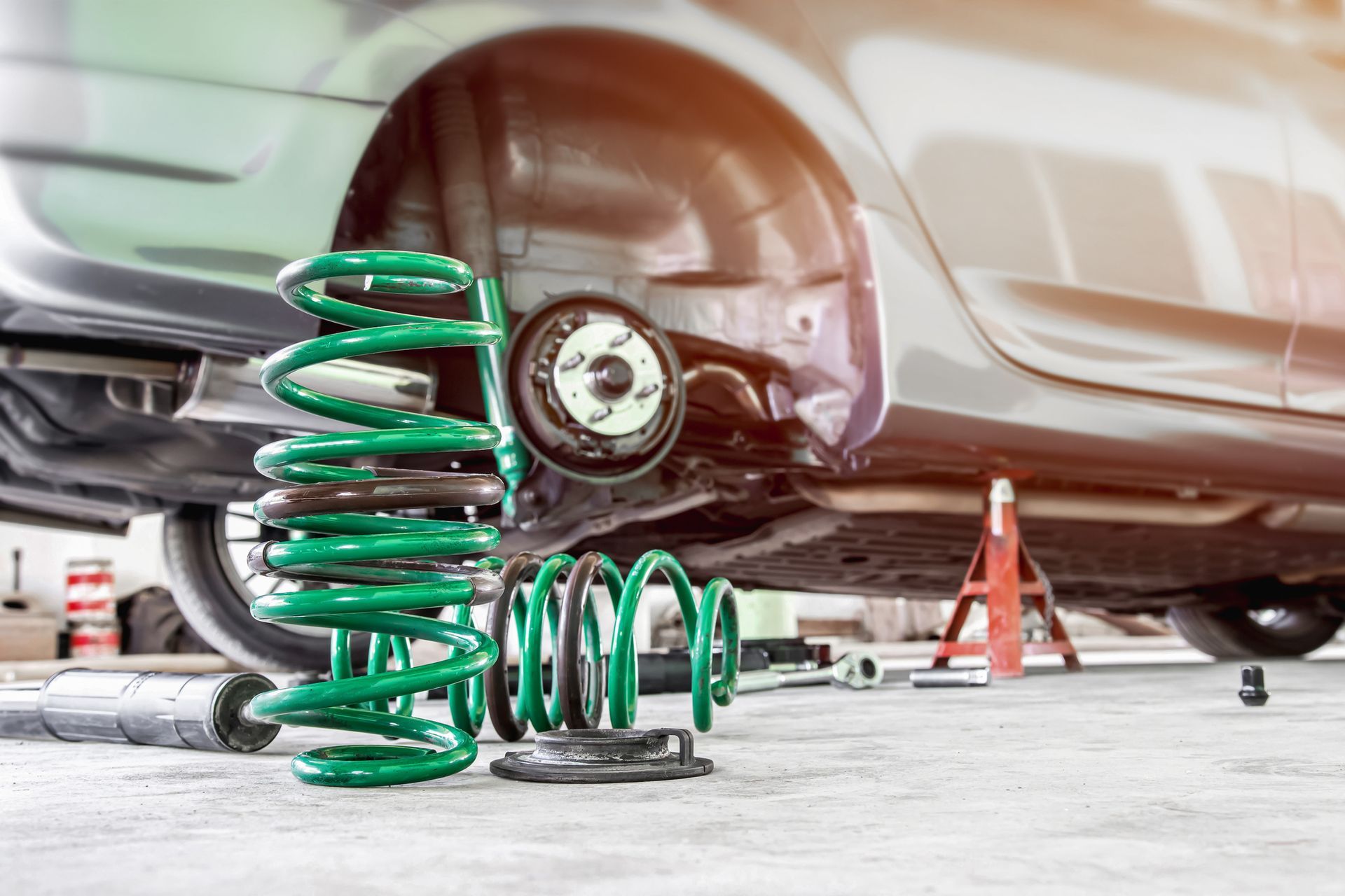 Car on jack stands with wheel removed, green coil springs and suspension parts laid out for repair