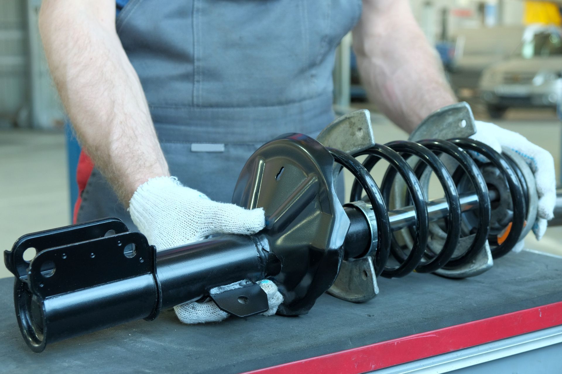 Mechanic holding a black car suspension strut with coil spring on a workbench