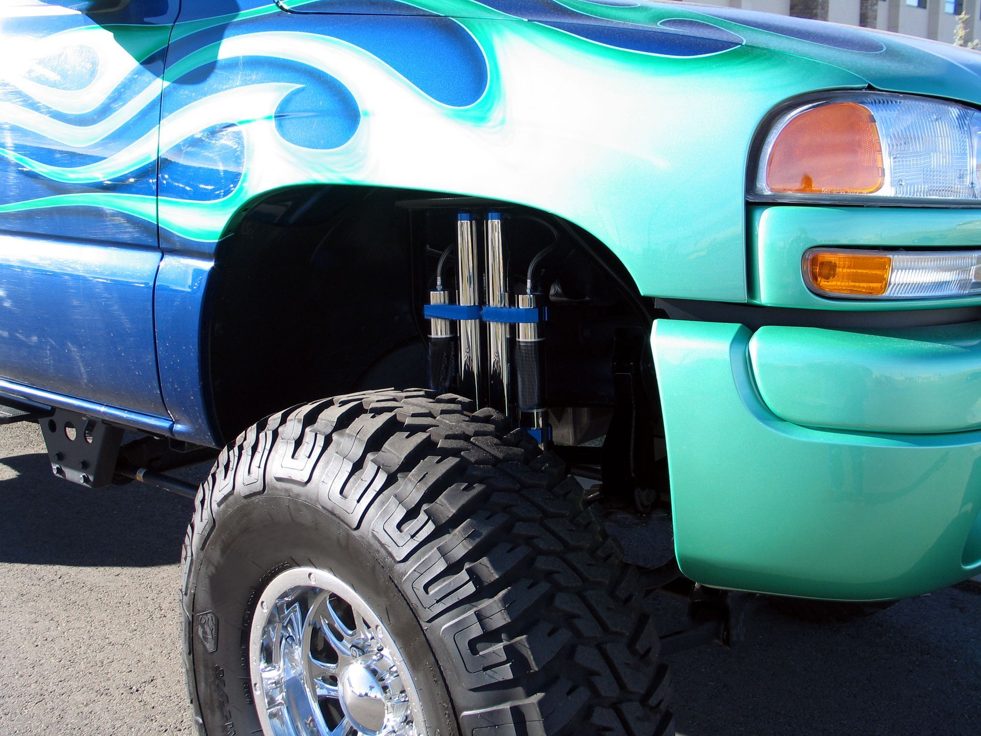Lifted teal-and-blue truck with oversized front tire and exposed suspension