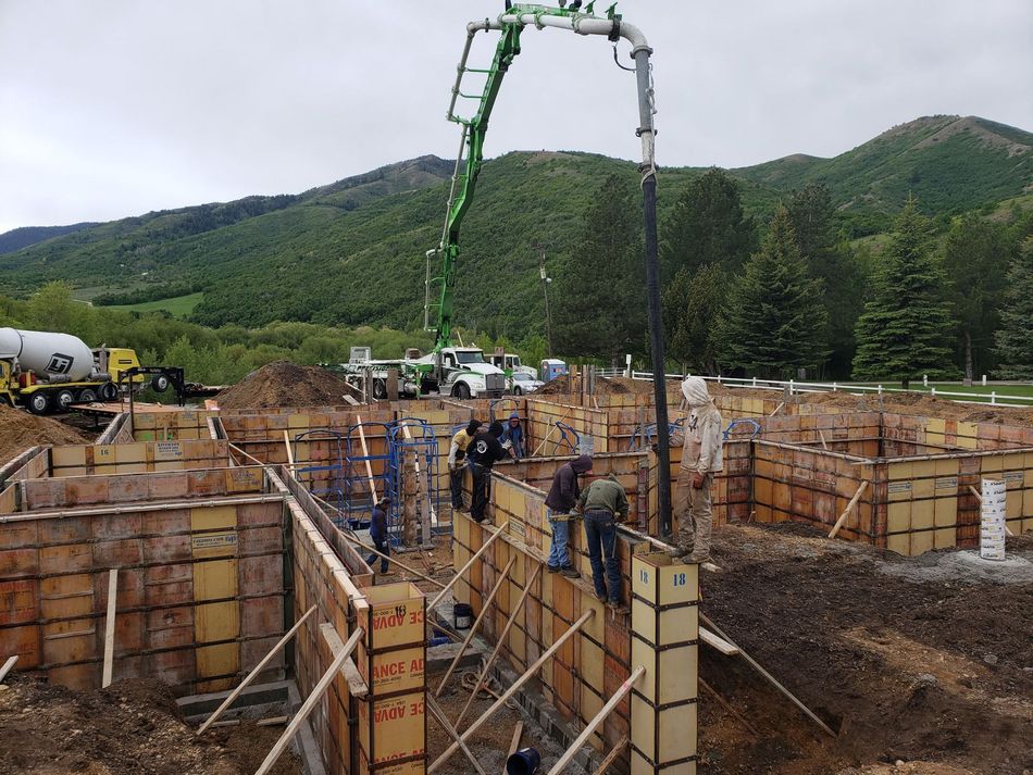 Construction site with workers pouring concrete over foundation walls, mountains in the background