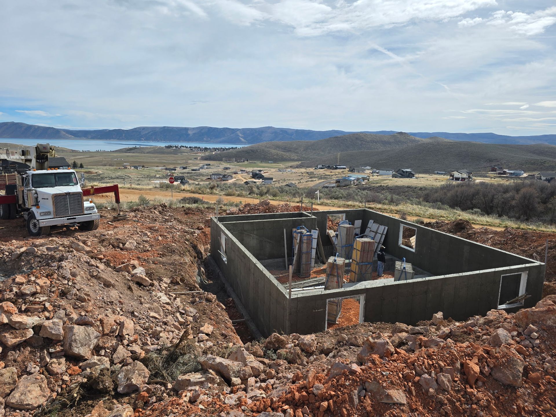 Construction site with concrete foundation walls in a rocky landscape and a truck nearby under cloudy sky