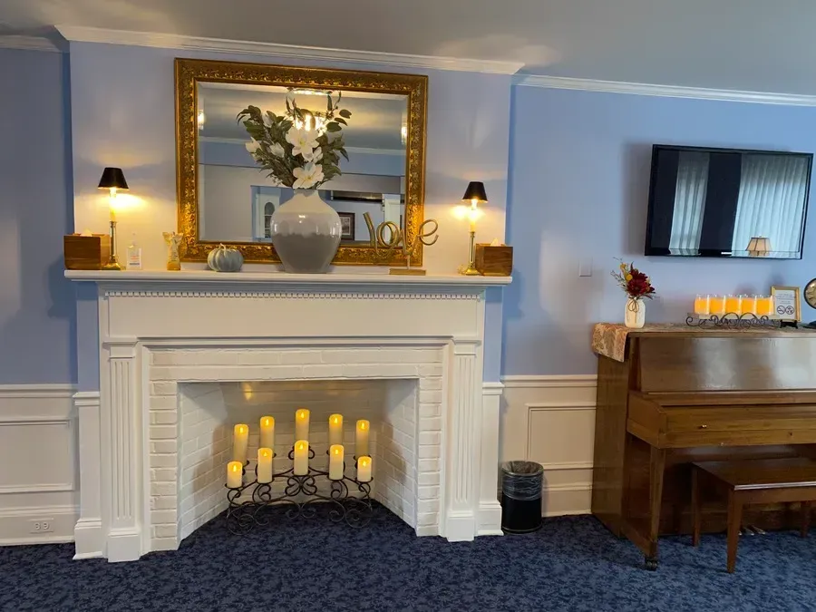 Elegant living room with white fireplace, gold mirror, lit candles, and a piano beneath a wall-mounted TV