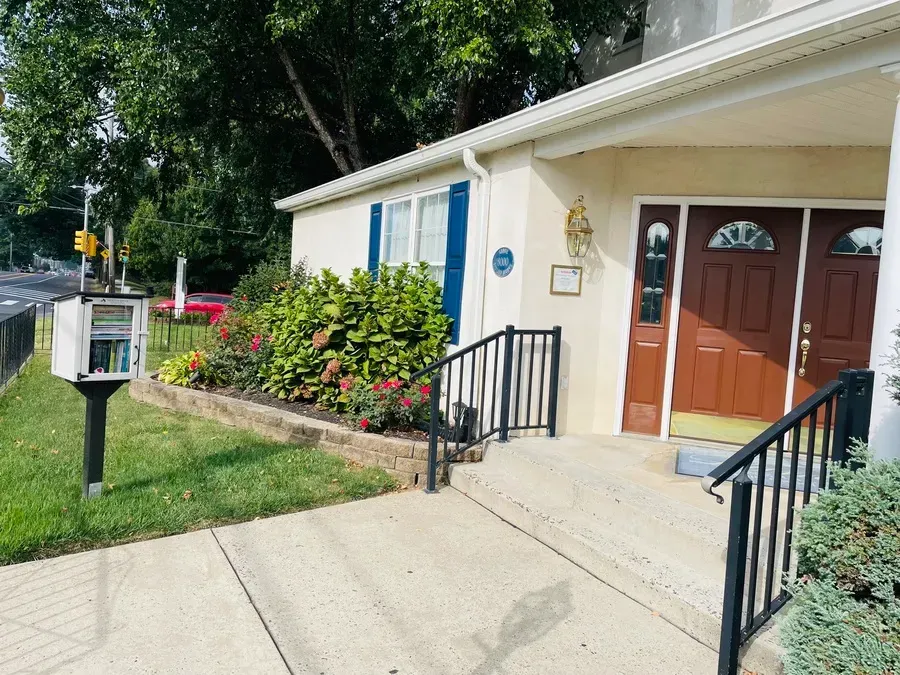 Exterior entrance to a building with double wooden doors, ramp, handrails, and flower beds in front