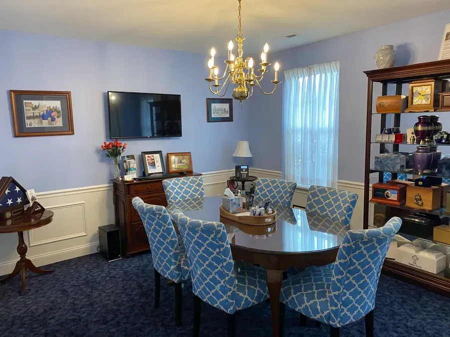 Dining room with blue walls, chandelier, oval table, patterned chairs, and TV on a sideboard.