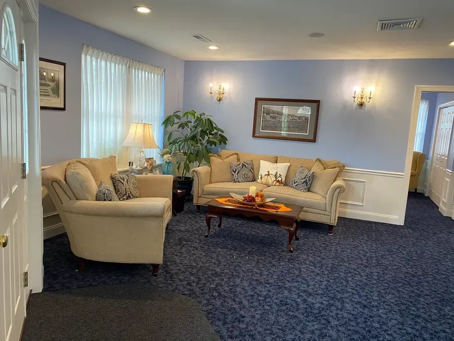 A cozy living room with beige sofas, blue carpet, lamps, and a coffee table in front of a window.