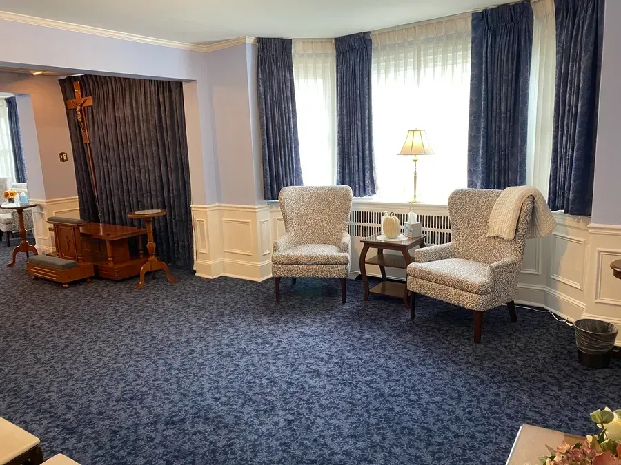 Quiet lounge with two armchairs, side table, lamp, blue carpet, and curtained windows
