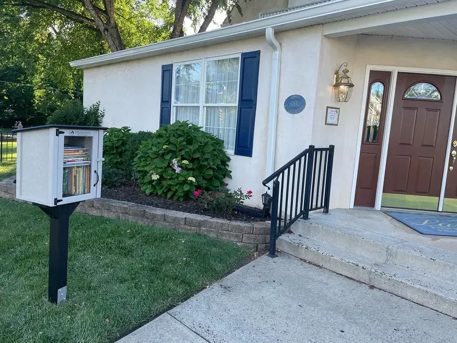 Mail receptacle beside a house entrance with a concrete walkway, steps, and blue shutters.