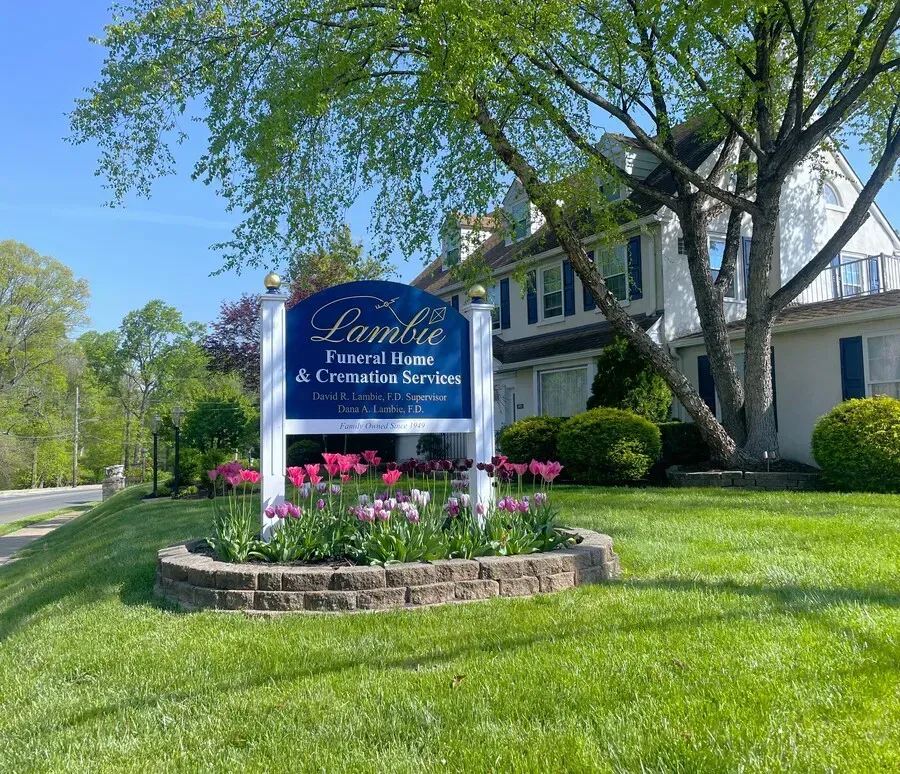 Blue sign for “Family Promise House & Connection Center” in front of a white building and flowers
