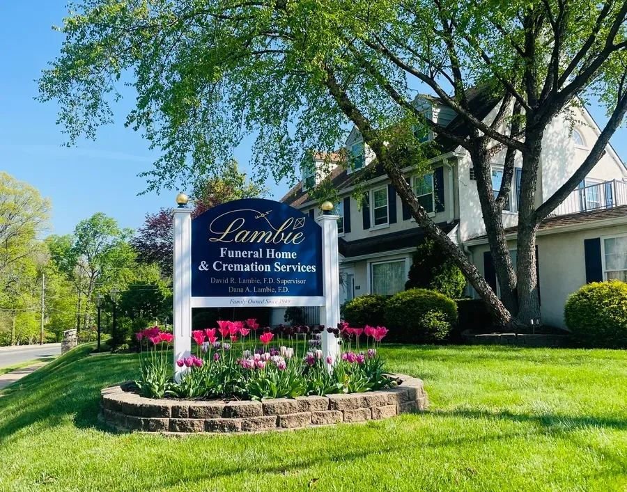 Sign for a bed-and-breakfast with pink flowers, green lawn, and trees in front of a house