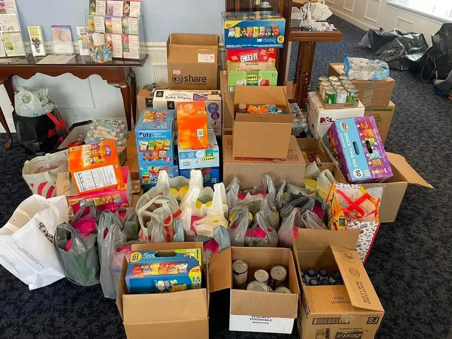 Packed room with boxed donations, gift bags, and assorted supplies arranged on the floor and tables.