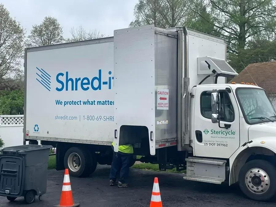 Shred-it garbage truck beside two trash bins and traffic cones outdoors
