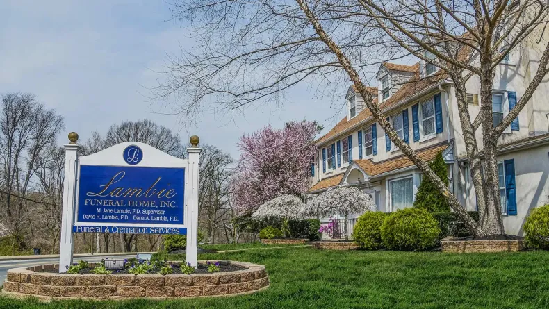 Blue-and-white business sign beside a landscaped brick building with trees and flowering bushes