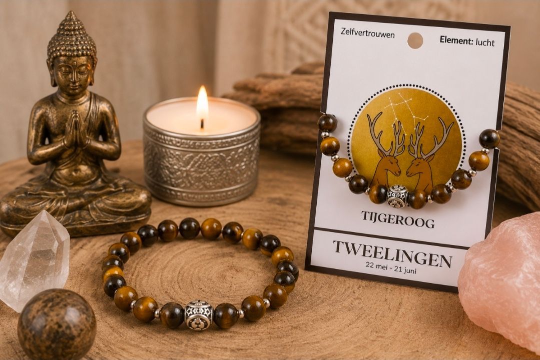 Een Boeddhabeeld, een brandende kaars, een kristal, een kralenarmband en een geel sieradenkaartje op een houten ondergrond.