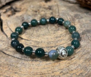 Een brandende kaars naast een agaat mala-kaart en een groene kralenarmband op een rustieke houten ondergrond.