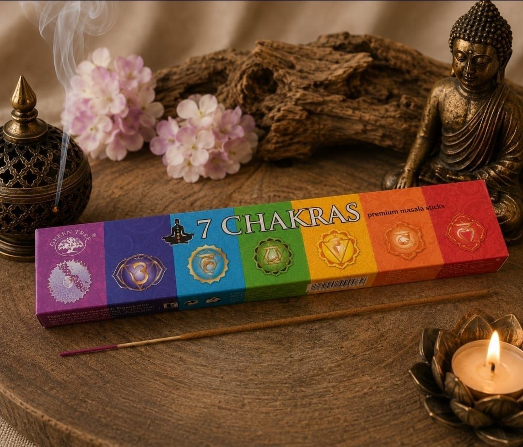 Een doosje met regenboogchakra-wierook naast een Boeddhabeeld, roze bloemen en een brandende kaars op een houten tafel.
