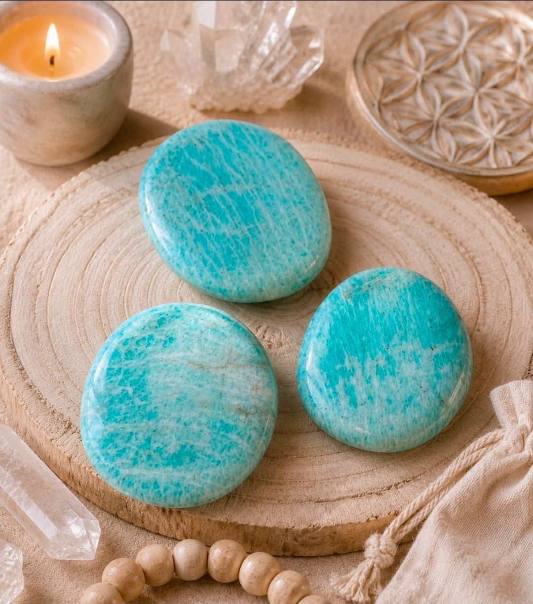 Drie turquoise stukken zeep op een geweven matje naast een kaars en houten kralen.