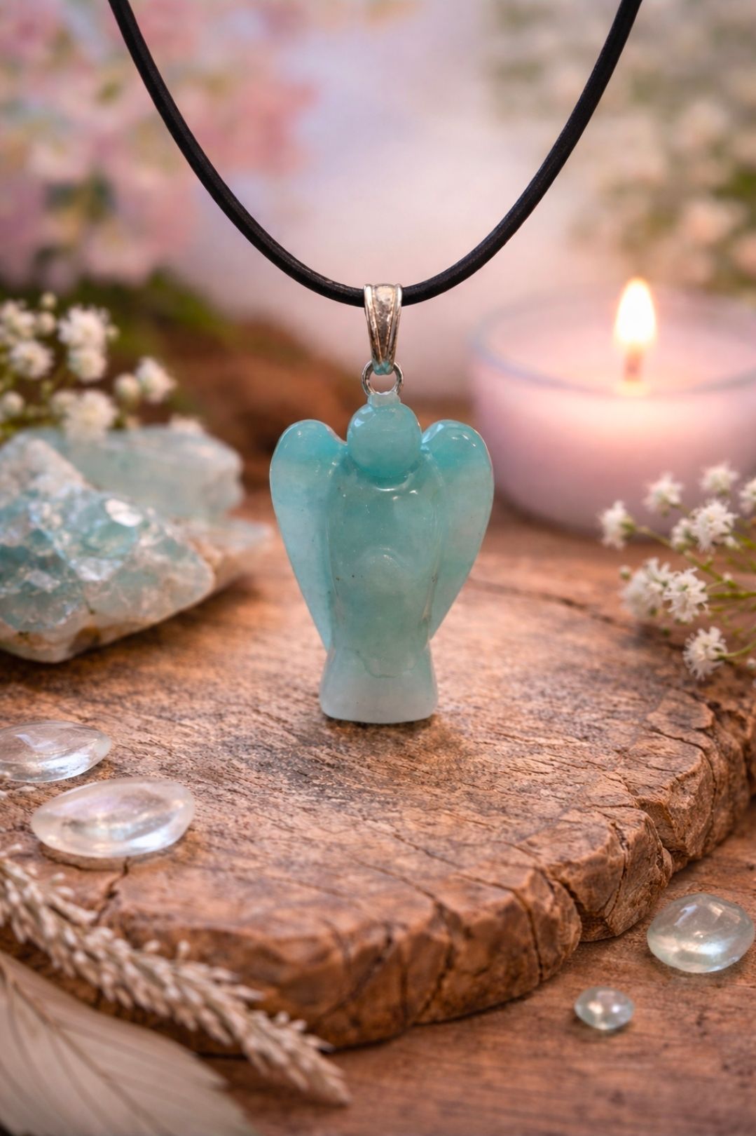 Een turquoise engelhanger aan een zwart koord, naast een brandende kaars op een rustieke houten plank.