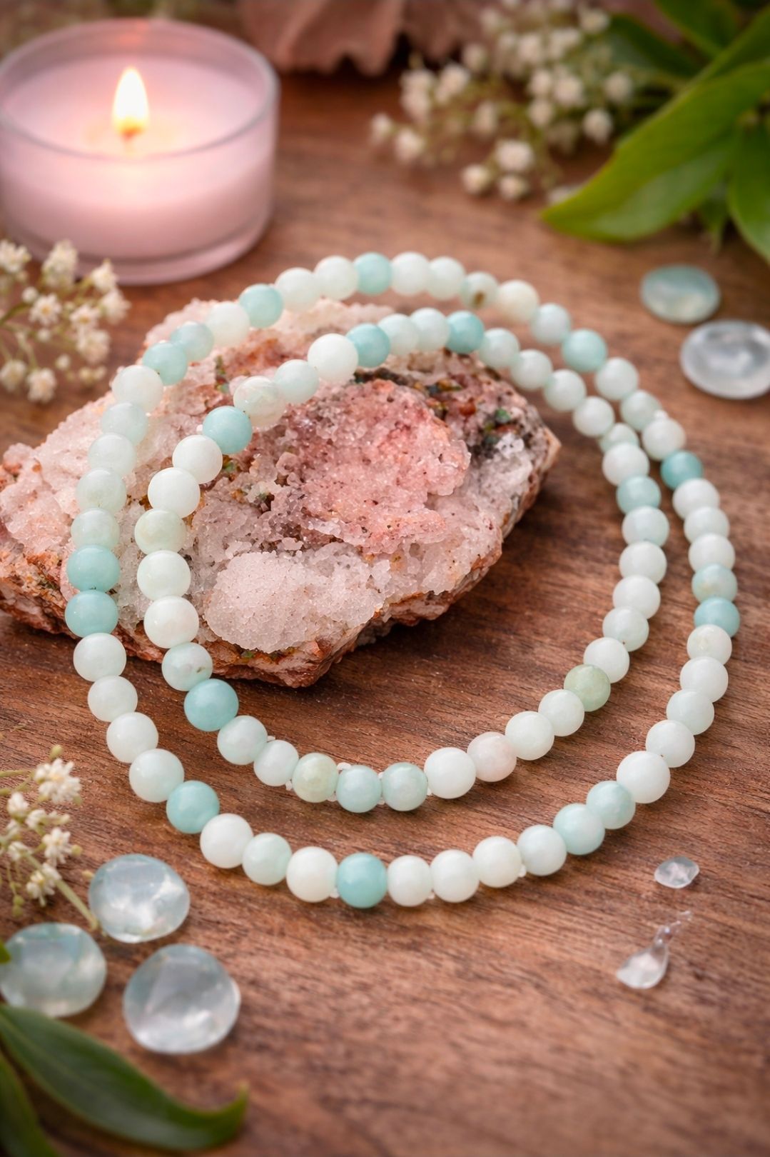 Pastelkleurige kralenarmbanden op een kristallen hanger met een brandende kaars op een houten ondergrond.