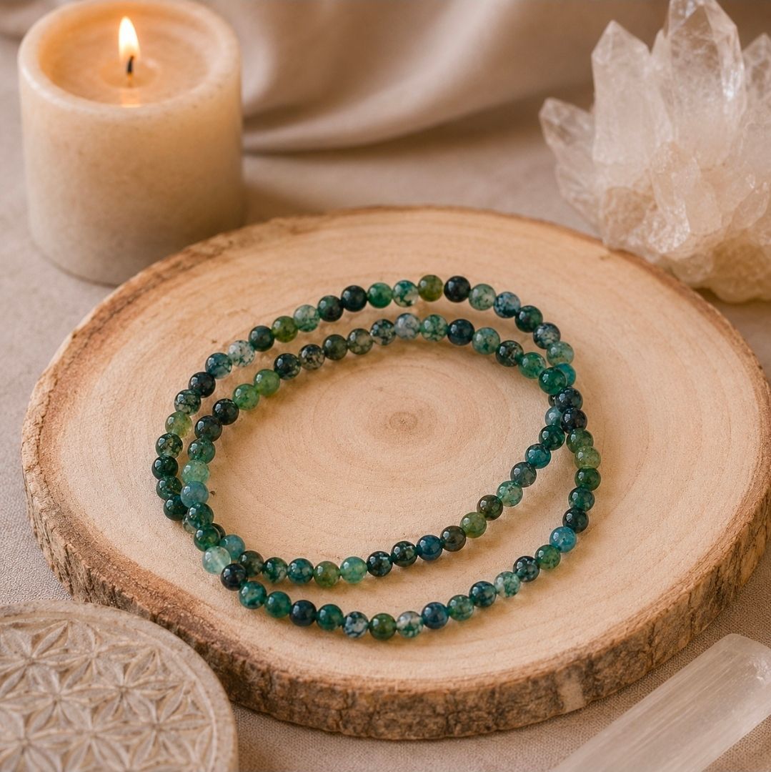 Groene kralenarmbandjes op een houten schijfje naast een brandende kaars en een helder kristal.