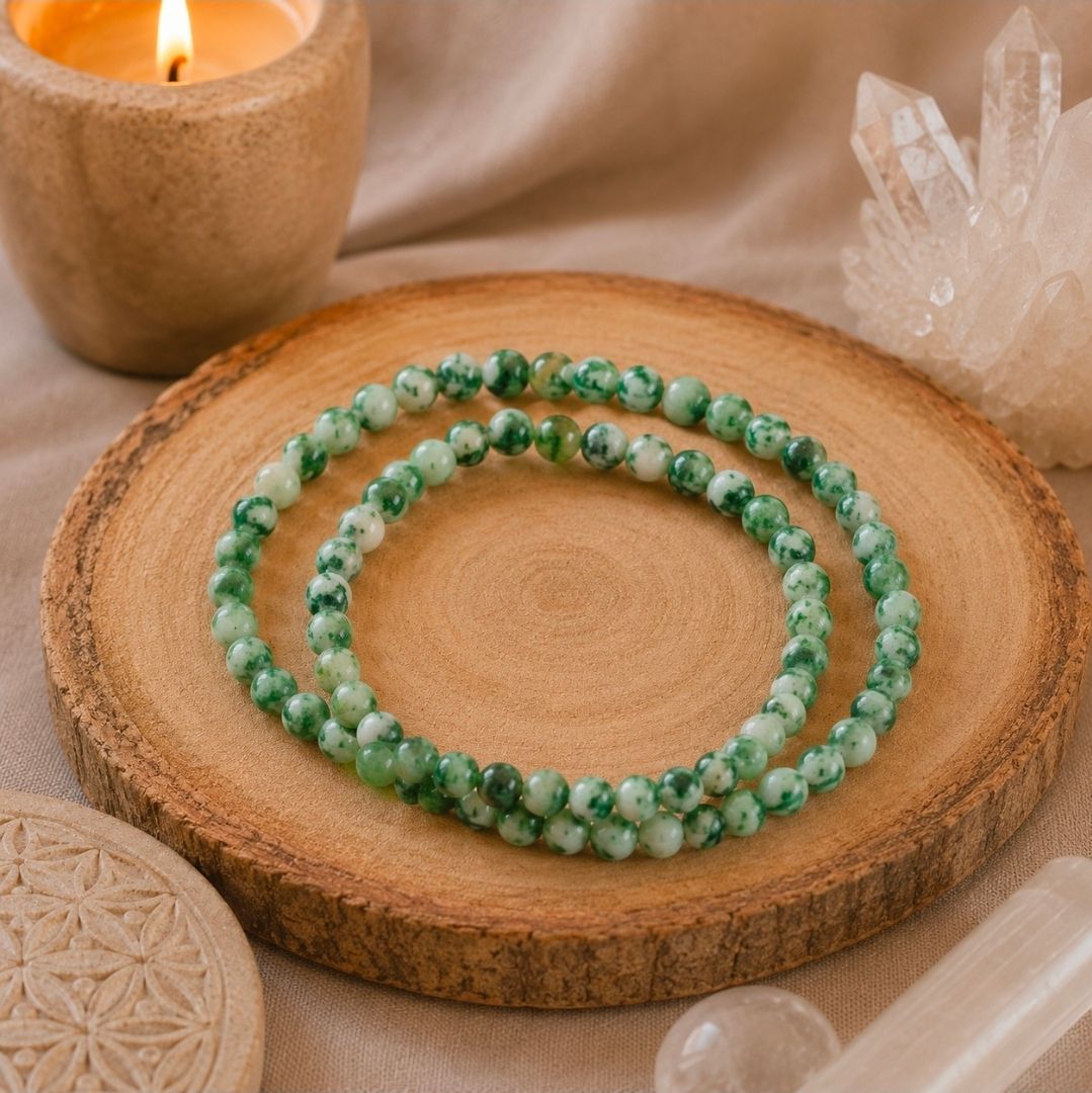 Groene kralenketting aan een houten schijfje naast een kaars en kristallen decoratie.