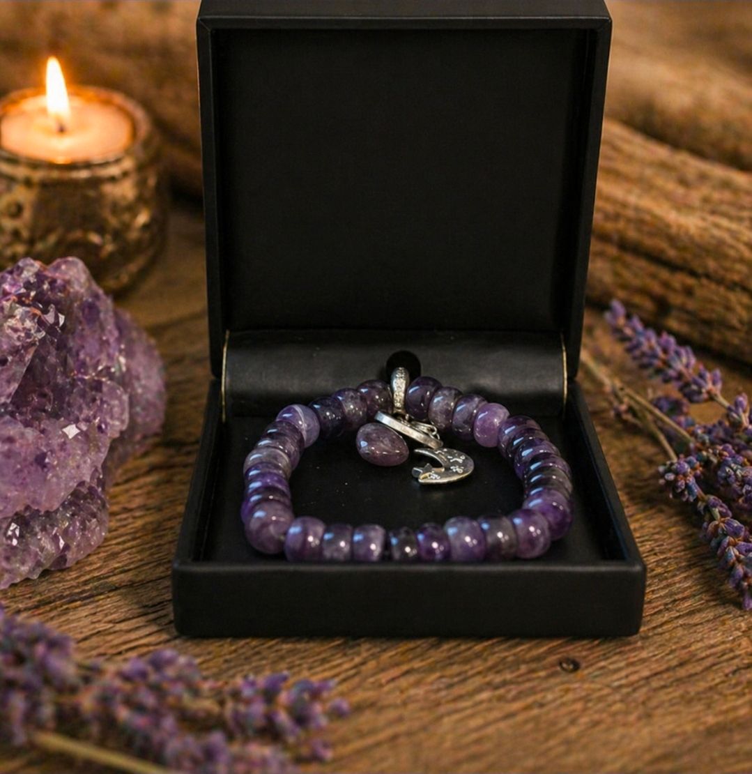 Een paarse kralenarmband in een open zwarte doos op een houten tafel met lavendel en een brandende kaars.