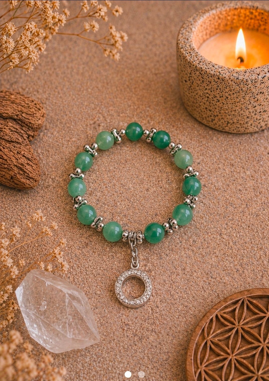 Groene kralenarmband met zilveren hanger op een warme, gestructureerde ondergrond naast een kristal en een brandende kaars.