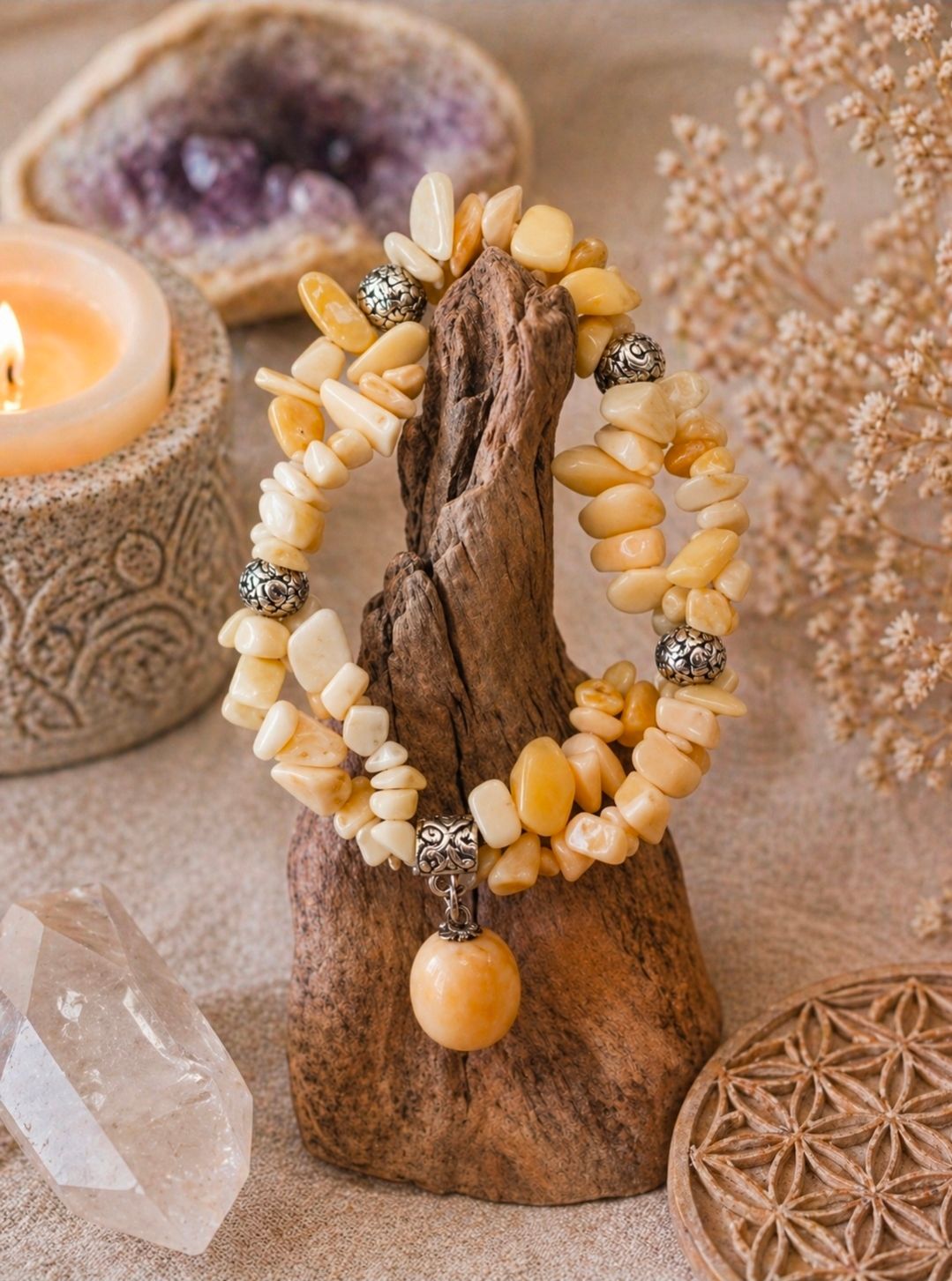 Armband van gele kralen op een houten standaard met kristallen en kaarsen in een warme, natuurlijke omgeving.