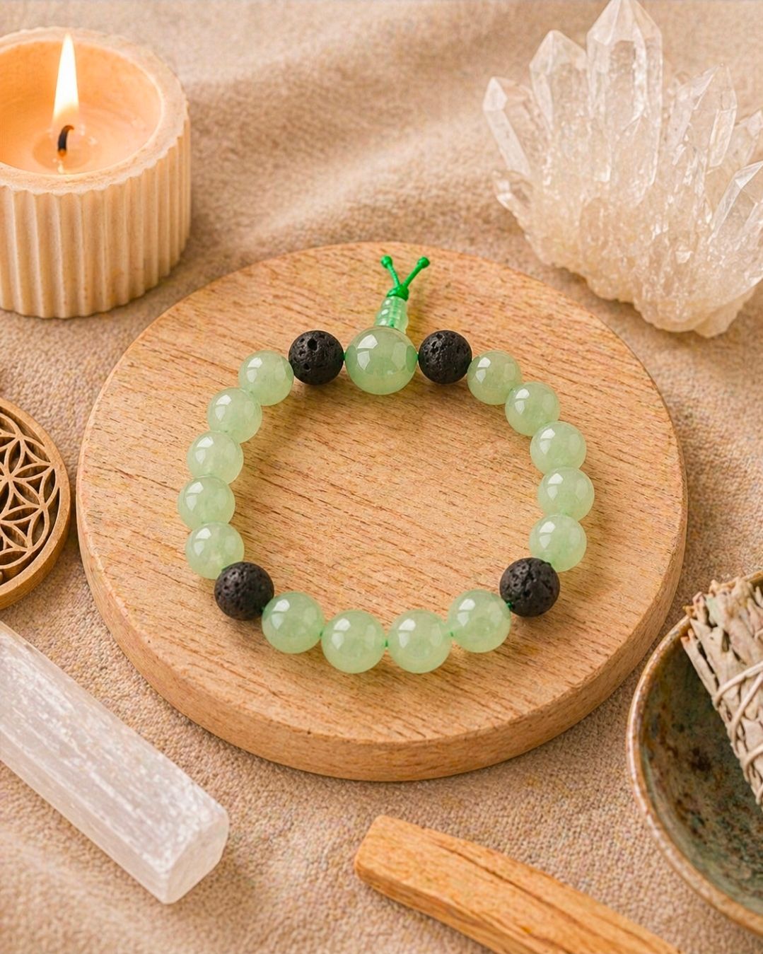 Groene kralenarmband met zwarte accenten op een rond houten dienblad, omringd door kaarsen en kristallen.
