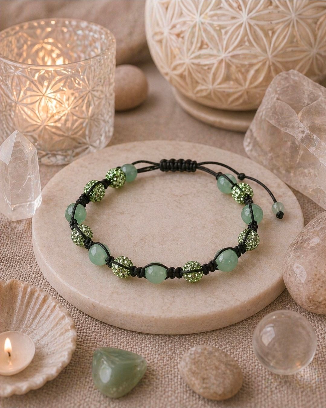 Groene kralenarmband op een stenen voetstuk met kristallen versiering en kaarslicht.
