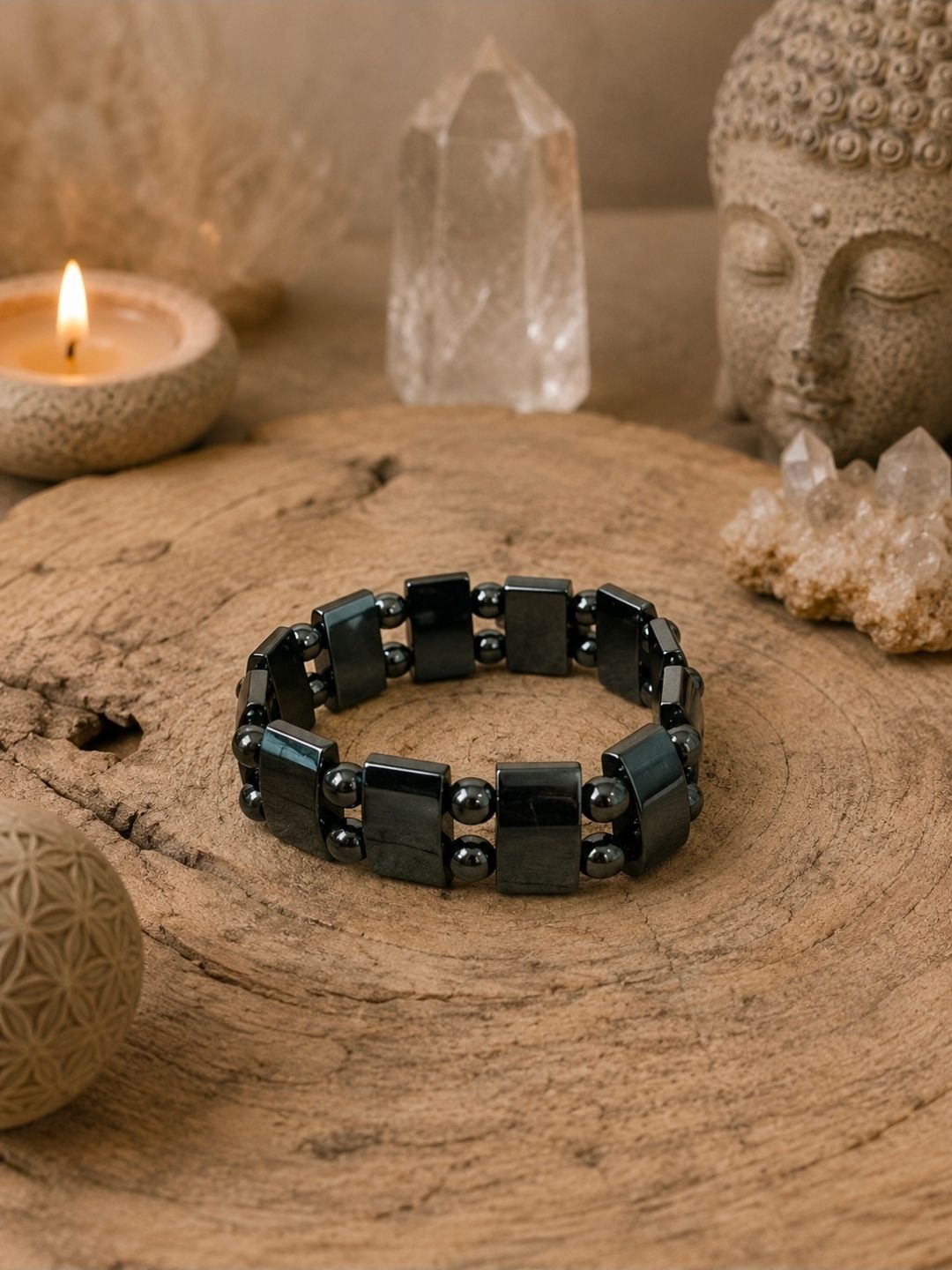 Een zwarte kralenarmband op een houten ondergrond met een brandende kaars, een kristal en een Boeddhabeeld op de achtergrond.