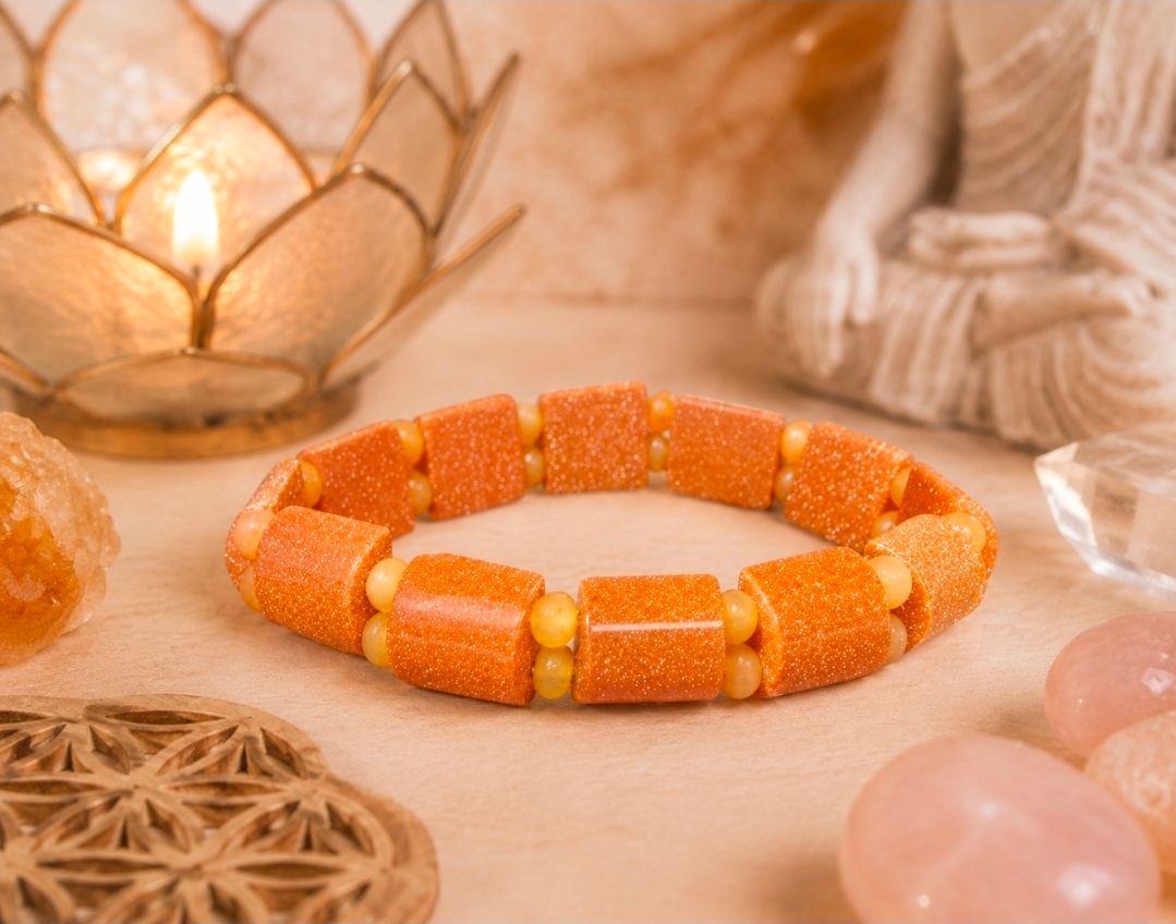 Een oranje kralenarmband op een sfeervol verlichte tafel met kaarsen en zachte decoratie.