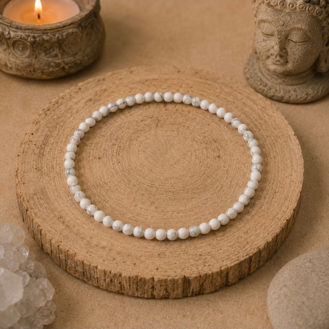 Witte kralenarmband op een ronde houten plaat met kaars, beeldje en kristallen decoratie op een beige achtergrond.